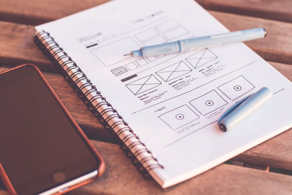 Boceto de wireframe de web en libreta junto a un smartphone